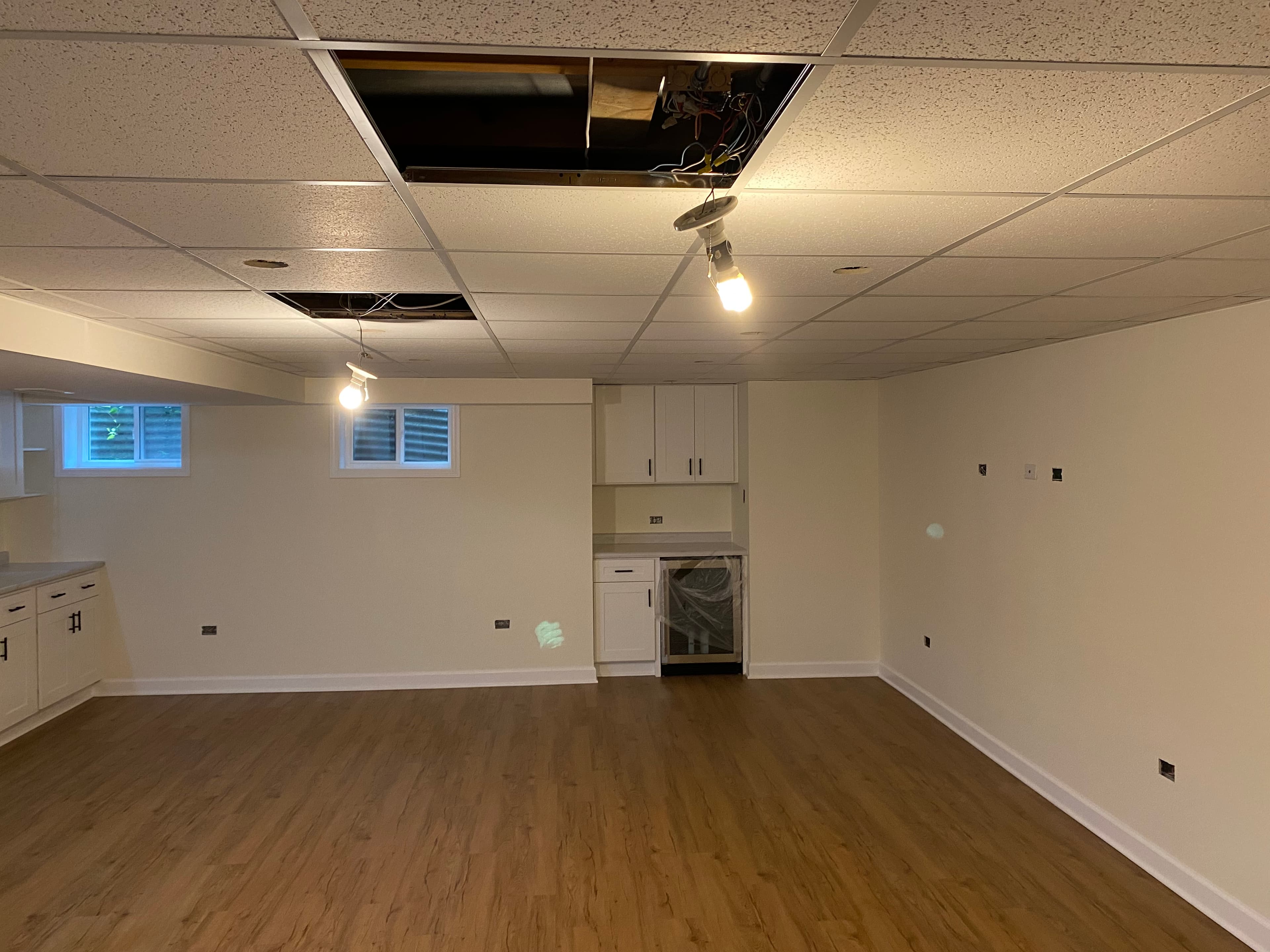 Basement renovation with new flooring and ceiling panels, with some ceiling openings still visible.