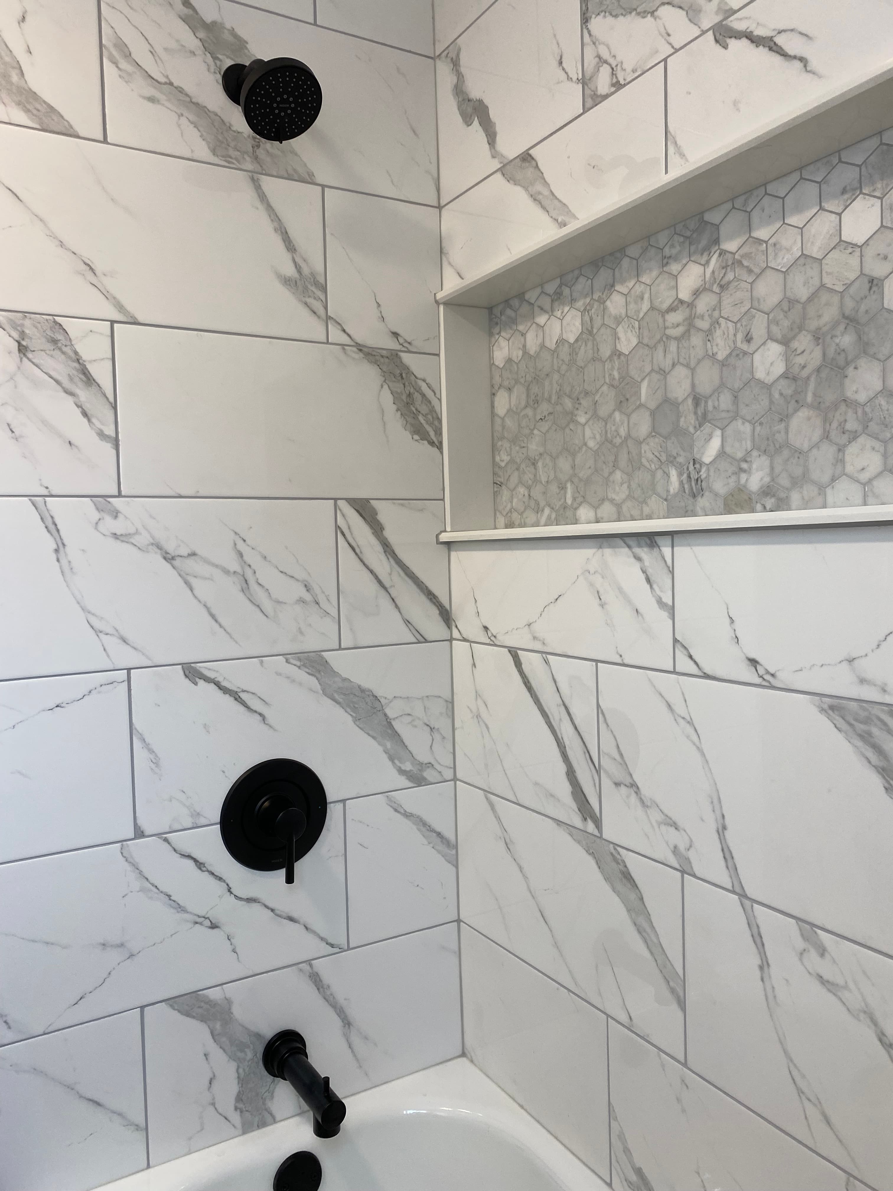 Marble-pattern shower tile, recessed mosaic niche and dark shower fittings.