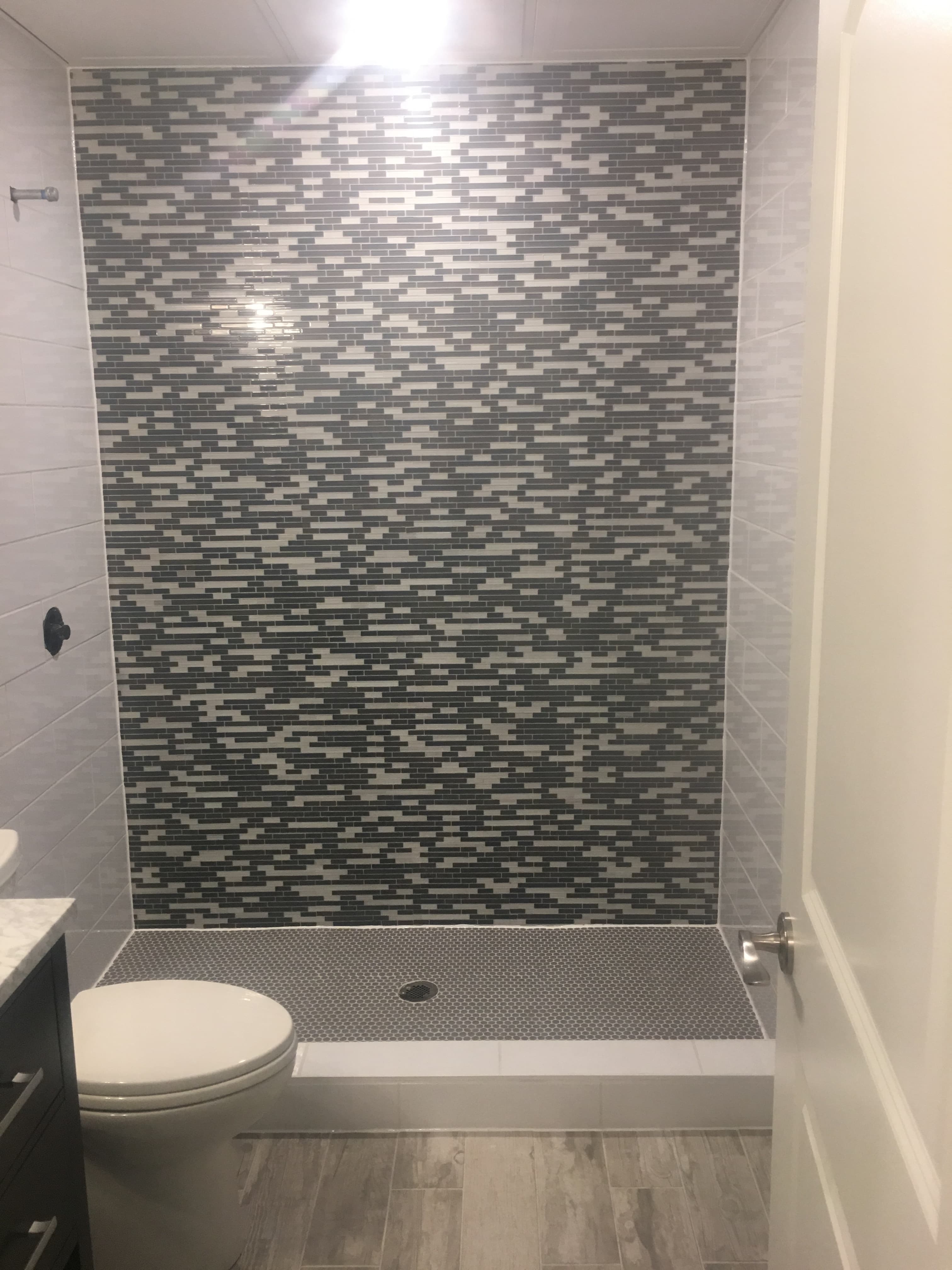 Bathroom with a patterned mosaic shower wall and glass enclosure.
