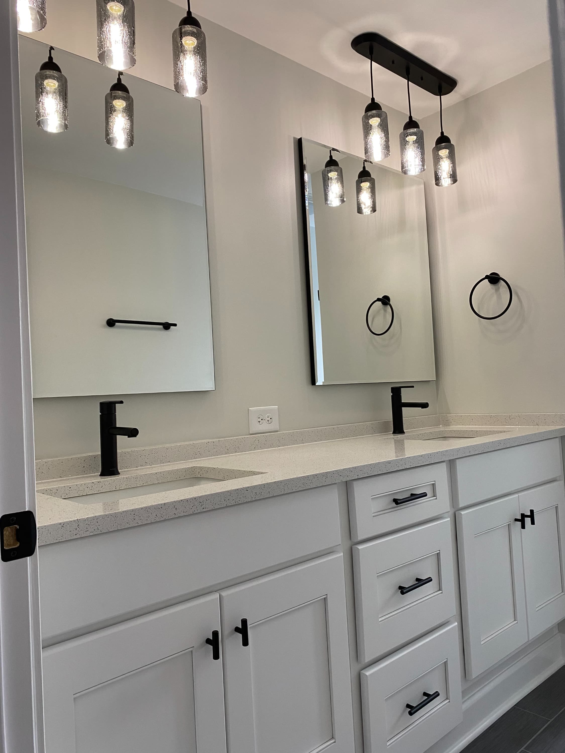 White double vanity with dark faucets and hardware, paired mirrors and pendant lighting.
