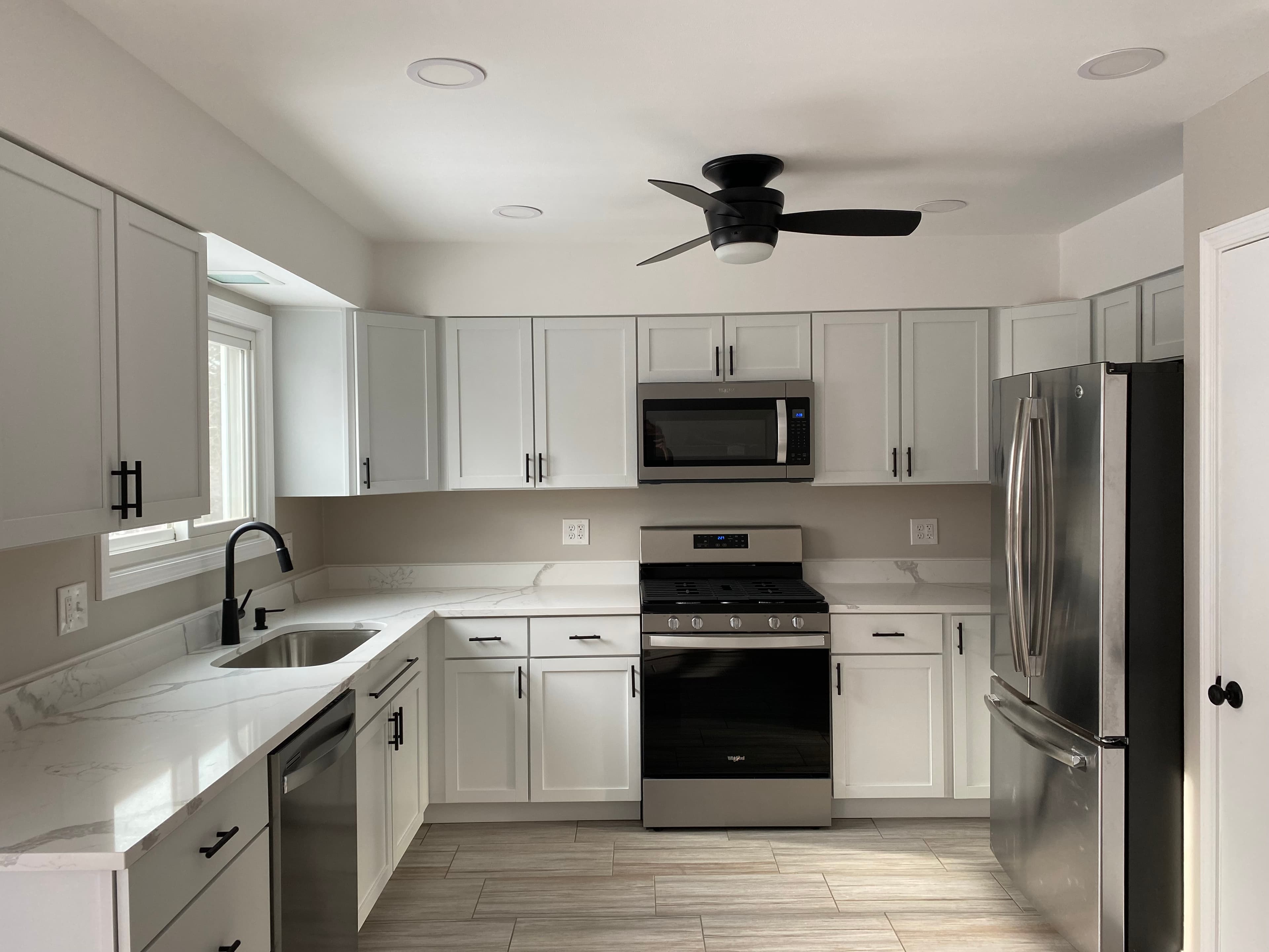 Remodeled kitchen with white cabinetry, dark hardware, pale counters and stainless steel appliances.