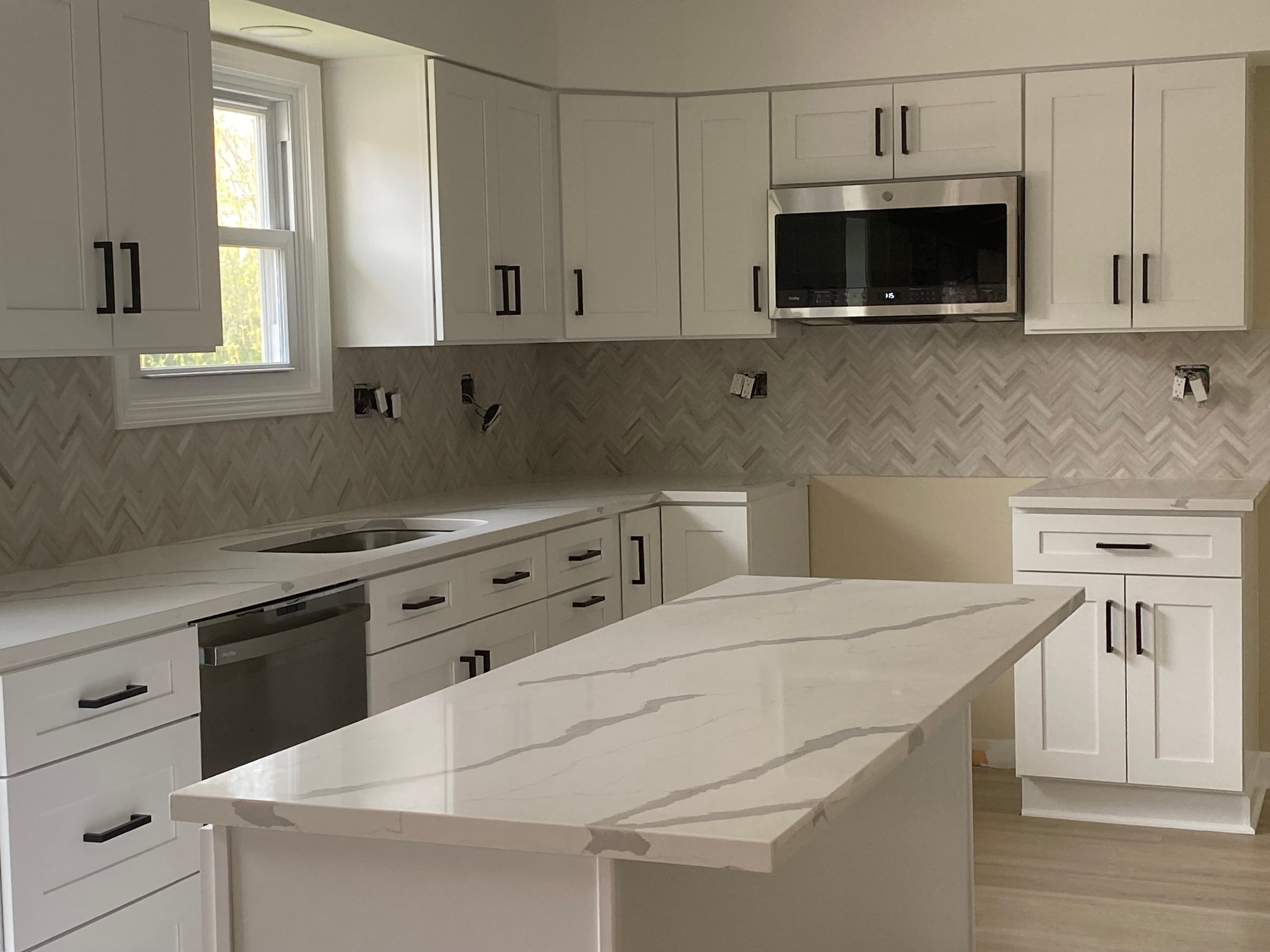 Kitchen renovation with white cabinetry, a pale island countertop and unfinished electrical fittings.