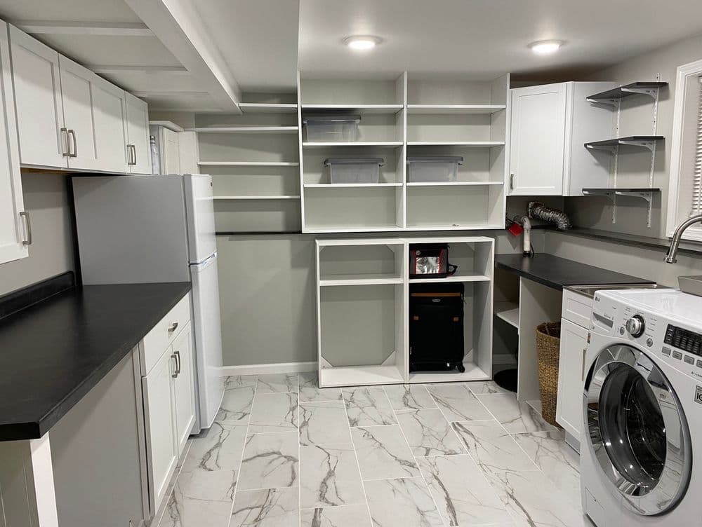 Laundry space with white cabinets, open shelving, dark counters and a washing machine.