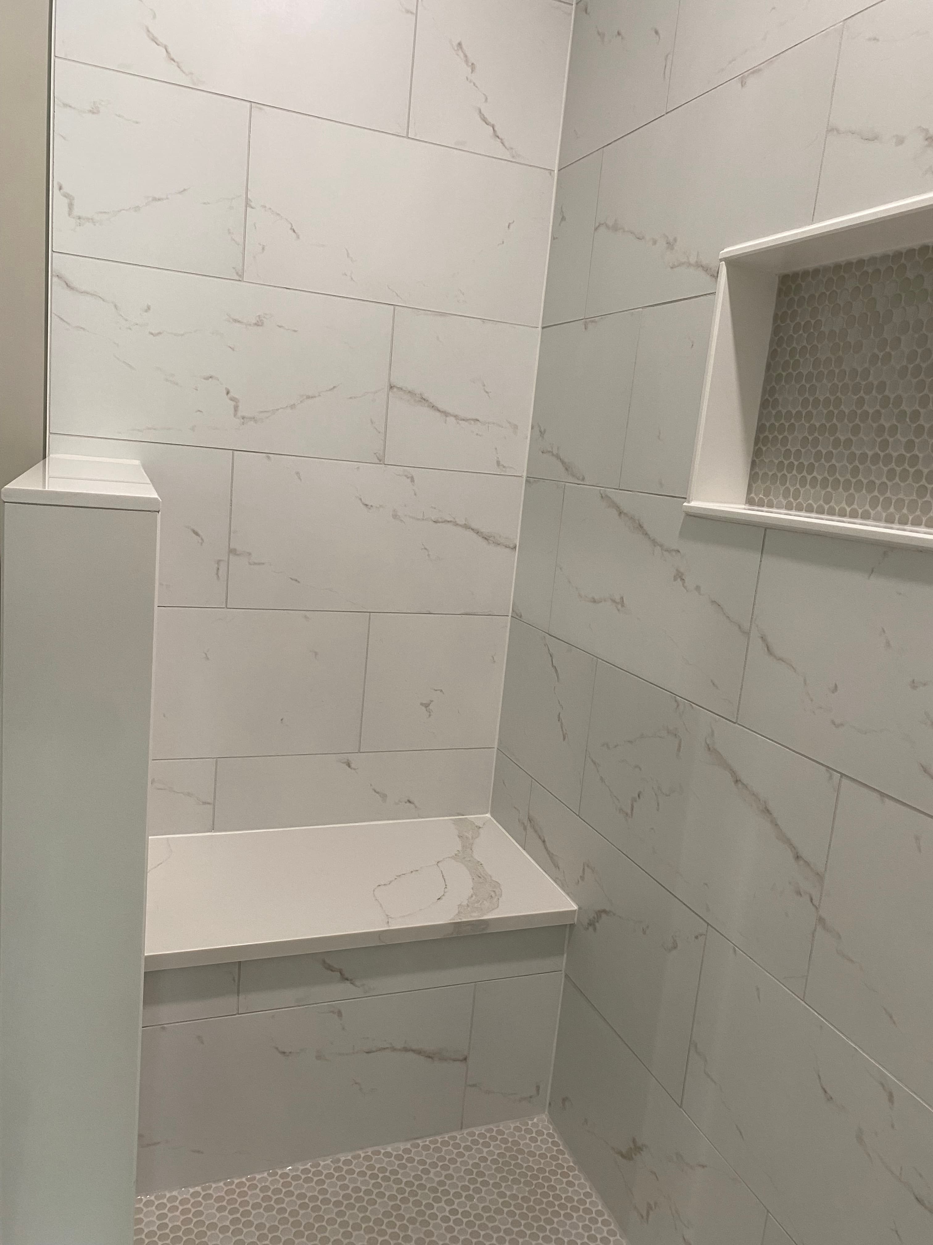 Pale tiled shower with a built-in bench and recessed shelf.