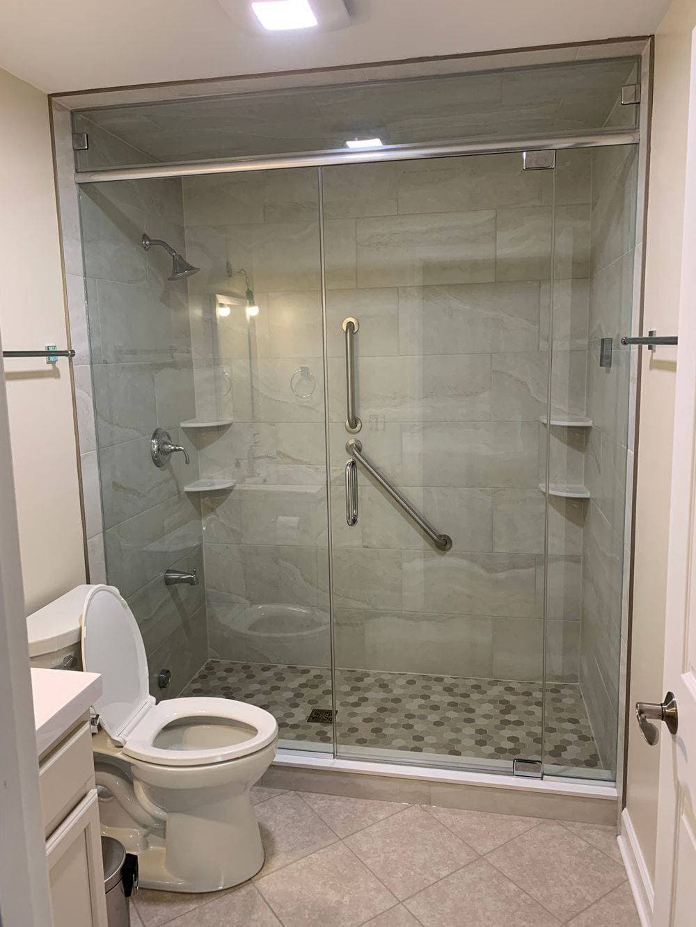 Glass shower enclosure with pale tile and a mosaic shower floor.